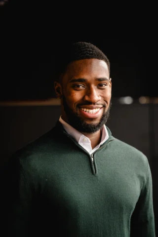 Smiling young man wearing green sweater looking directly at the camera